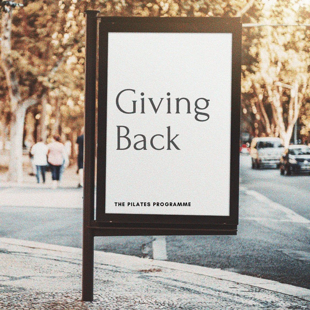 A Giving Back sign from The Pilates Programme on a tree-lined street